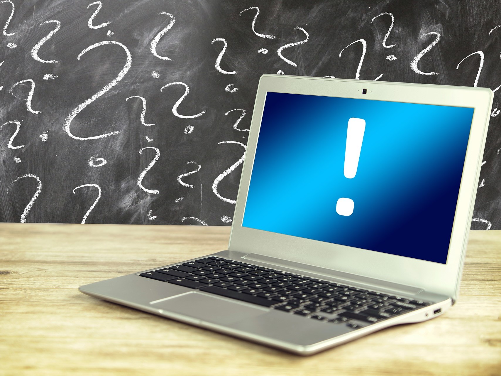 Auf einem Holzschreibtisch steht ein Laptop, auf dessen Bildschirm ein großes Ausrufezeichen angezeigt wird. Im Hintergrund ist eine Tafel voller Fragezeichen, oder „Fragen“, mit weißer Kreide gezeichnet, was die Neugier widerspiegelt, die man oft auf Pinterest-Boards findet.