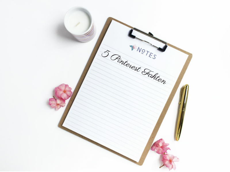 Ein Klemmbrett mit liniertem Papier mit der Aufschrift „Pinterest Fakten“ zeigt handschriftliche Notizen. Es liegt elegant auf einer weißen Oberfläche, die mit verstreuten rosa Blütenblättern geschmückt ist. Rechts daneben steht eine brennende Kerze in einem kleinen Gefäß und ein goldener Stift, was eine einladende und inspirierende Atmosphäre schafft.