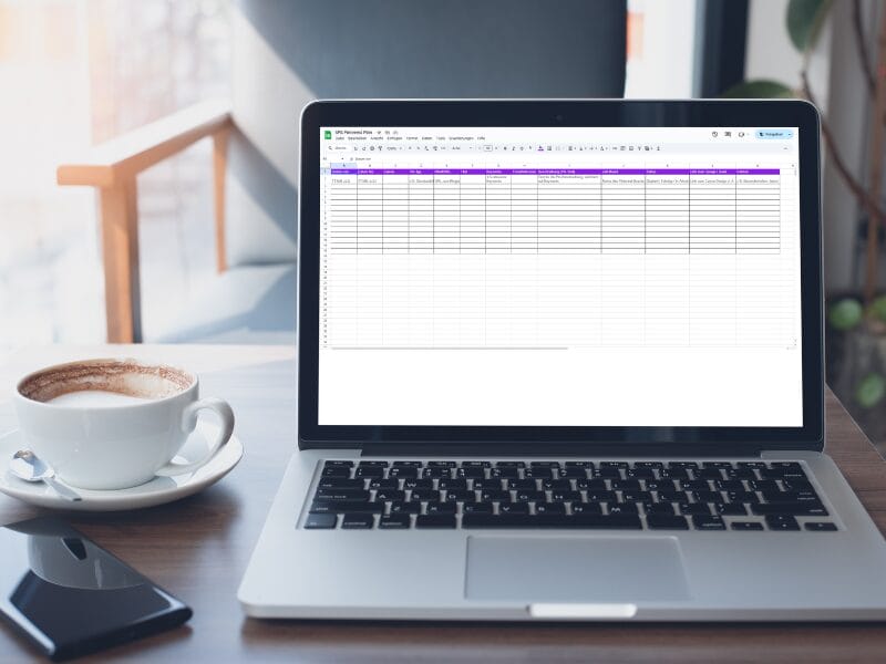 Ein Laptop auf einem Holztisch zeigt eine Workflow-Tabelle mit violetten Überschriften. Neben dem Laptop stehen eine Tasse Kaffee, eine Untertasse und eine kabellose Maus. Im Hintergrund sind ein Stuhl und ein Fenster mit Tageslicht zu sehen.