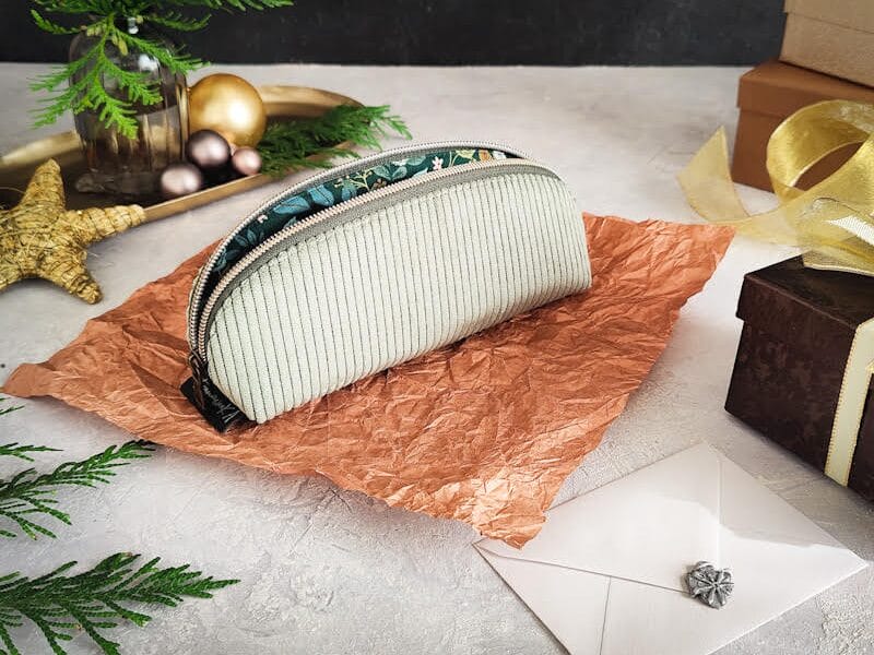 Gute Produktfotos für Pinterest gestalten 5 Ein kleiner, heller Beutel mit Reißverschluss liegt auf zerknittertem braunem Papier, umgeben von einem weißen Umschlag mit Wachssiegel, Geschenkkartons, einem goldenen Stern und festlichem Grün - perfekte Elemente für charmante Produktfotos.