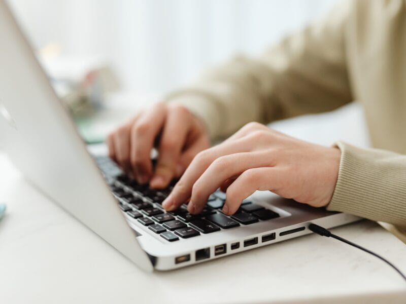 Warum auf Pinterest Follower nicht nötig sind 1 Nahaufnahme eines Anhängers, der an einem Schreibtisch auf einer Laptoptastatur tippt, wobei die Hände im Mittelpunkt stehen und der Bildschirm teilweise sichtbar ist. Die Person trägt ein helles, langärmeliges Oberteil.