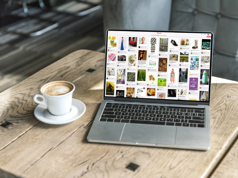 7 Zeichen einer veralteten Pinterest-Strategie 1 Auf einem Holztisch steht neben einer Tasse Kaffee ein Laptop, auf dem ein Feed zur Pinterest-Strategie angezeigt wird.